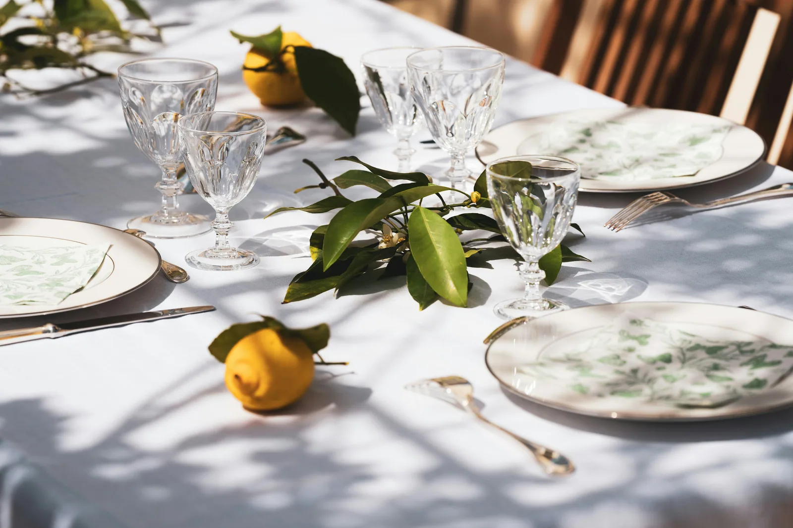 A table set with plates, crystal glasses, lemons, and green leaves in