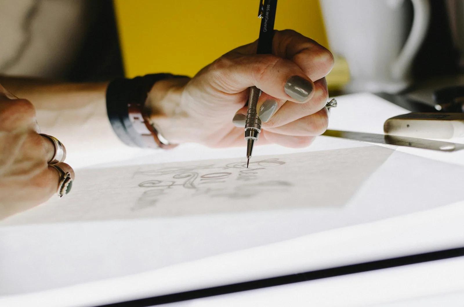 Person lettering on tracing paper using mechanical pencil