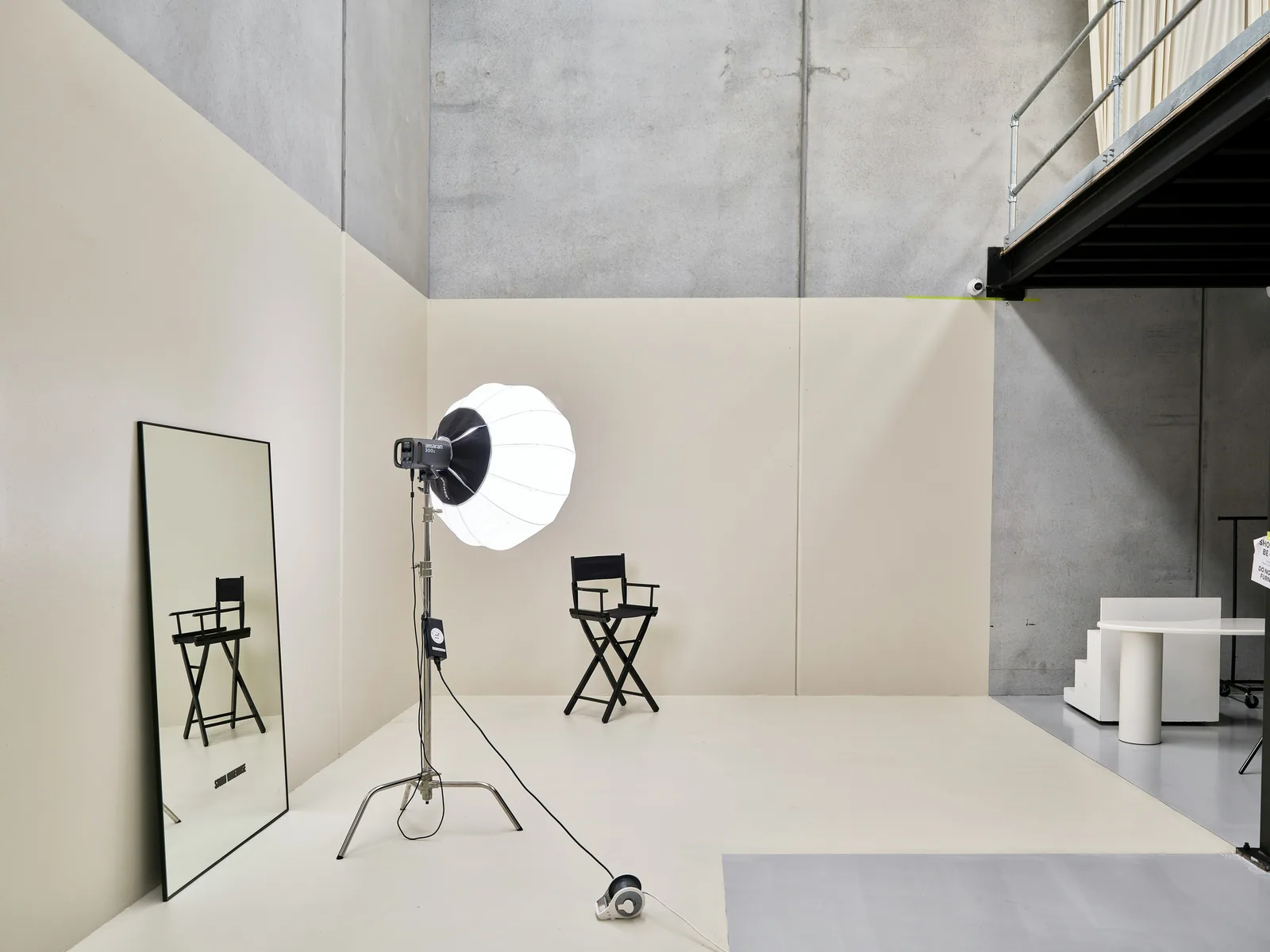 A black director chair, a studio light, and a tall mirror in a studio