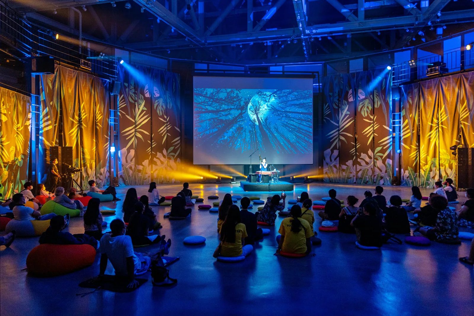 A stage in coloured light, with people on floor seating