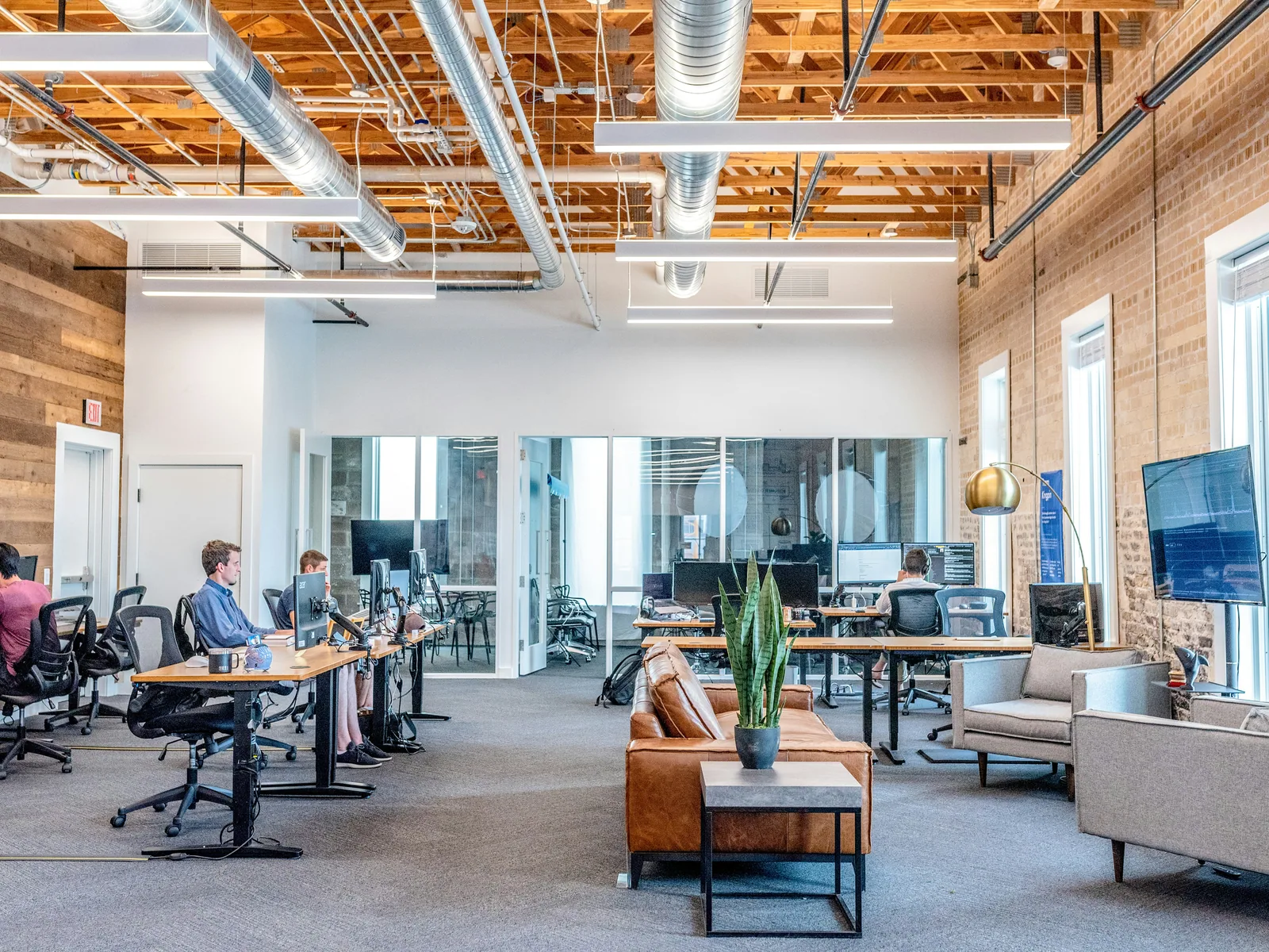 An open office with desks, a lounge corner and brick walls