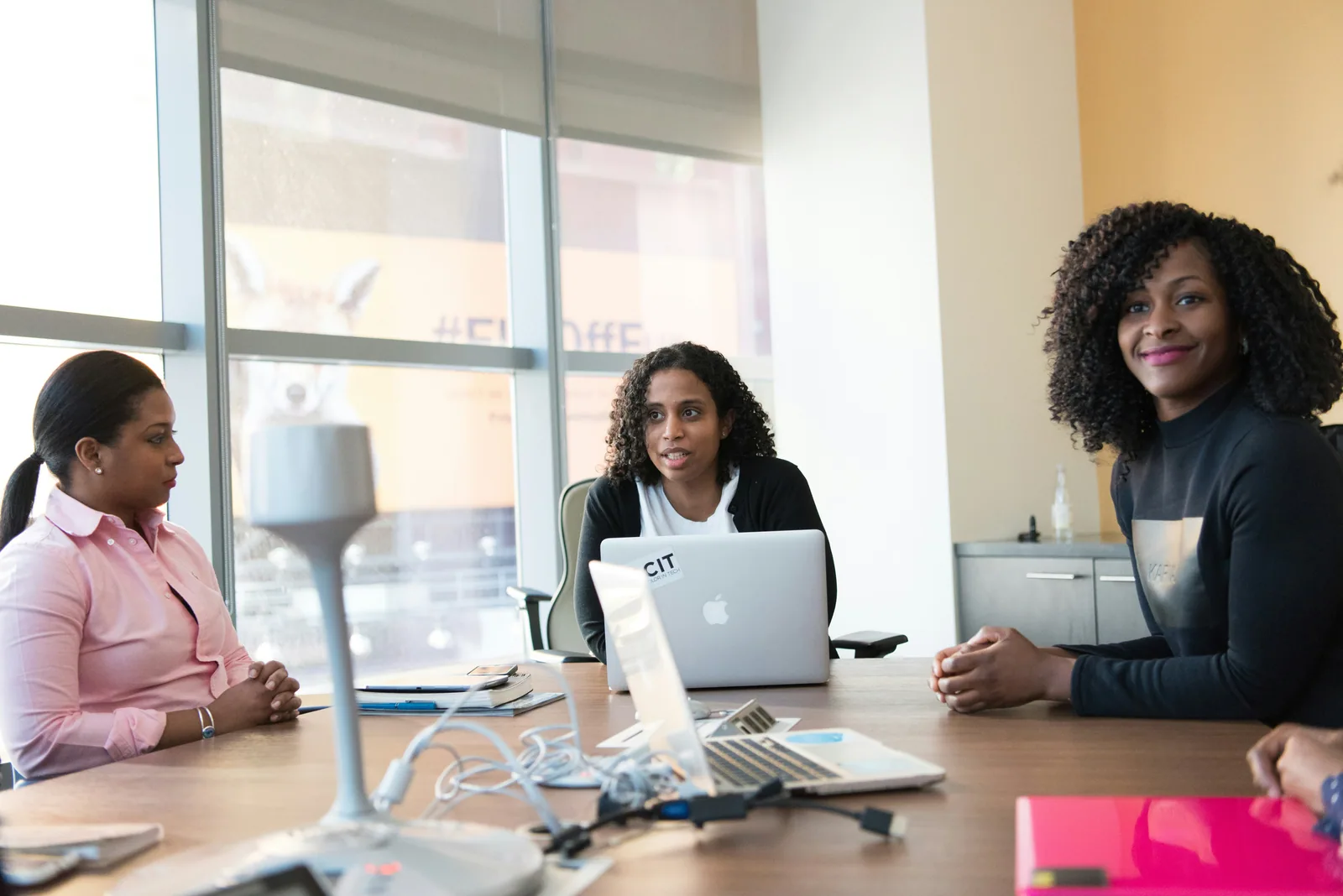 Three women in a meeting at a table by a tall window