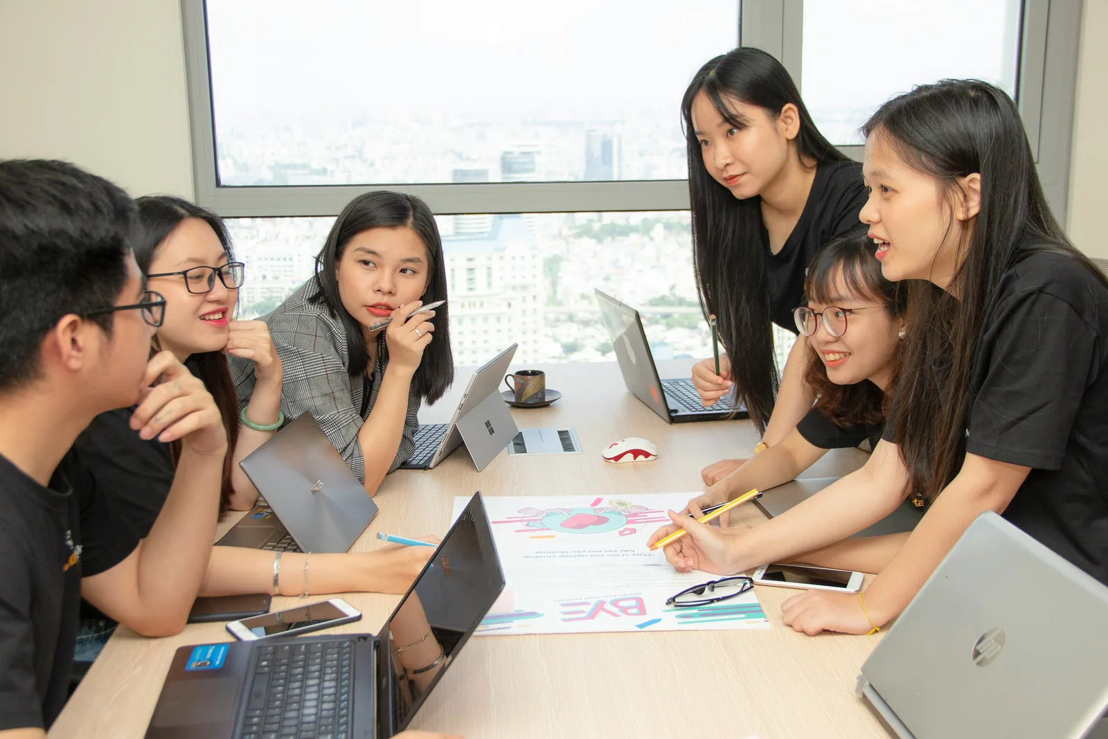 Five colleagues leaning over a table of laptops and notes