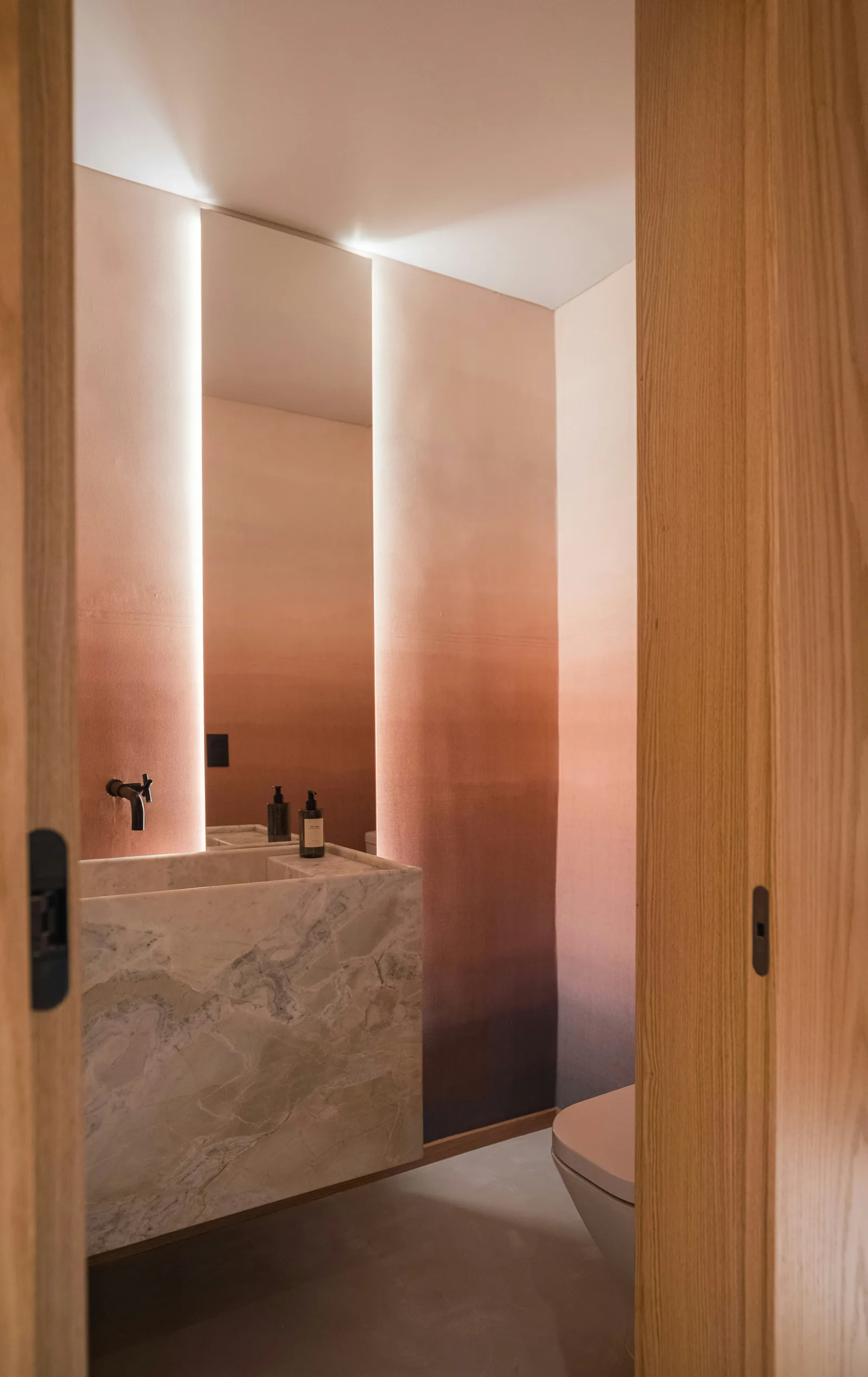 A bathroom with a marble basin and walls that fade from pink to brown