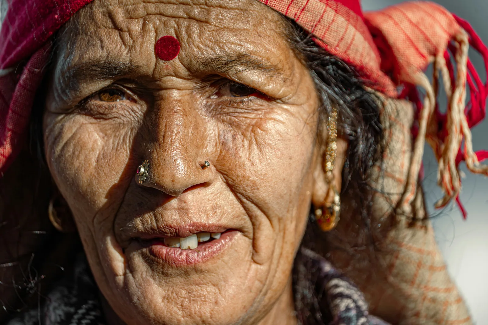 A close, bright colour portrait of an older woman in a red headscarf, smiling