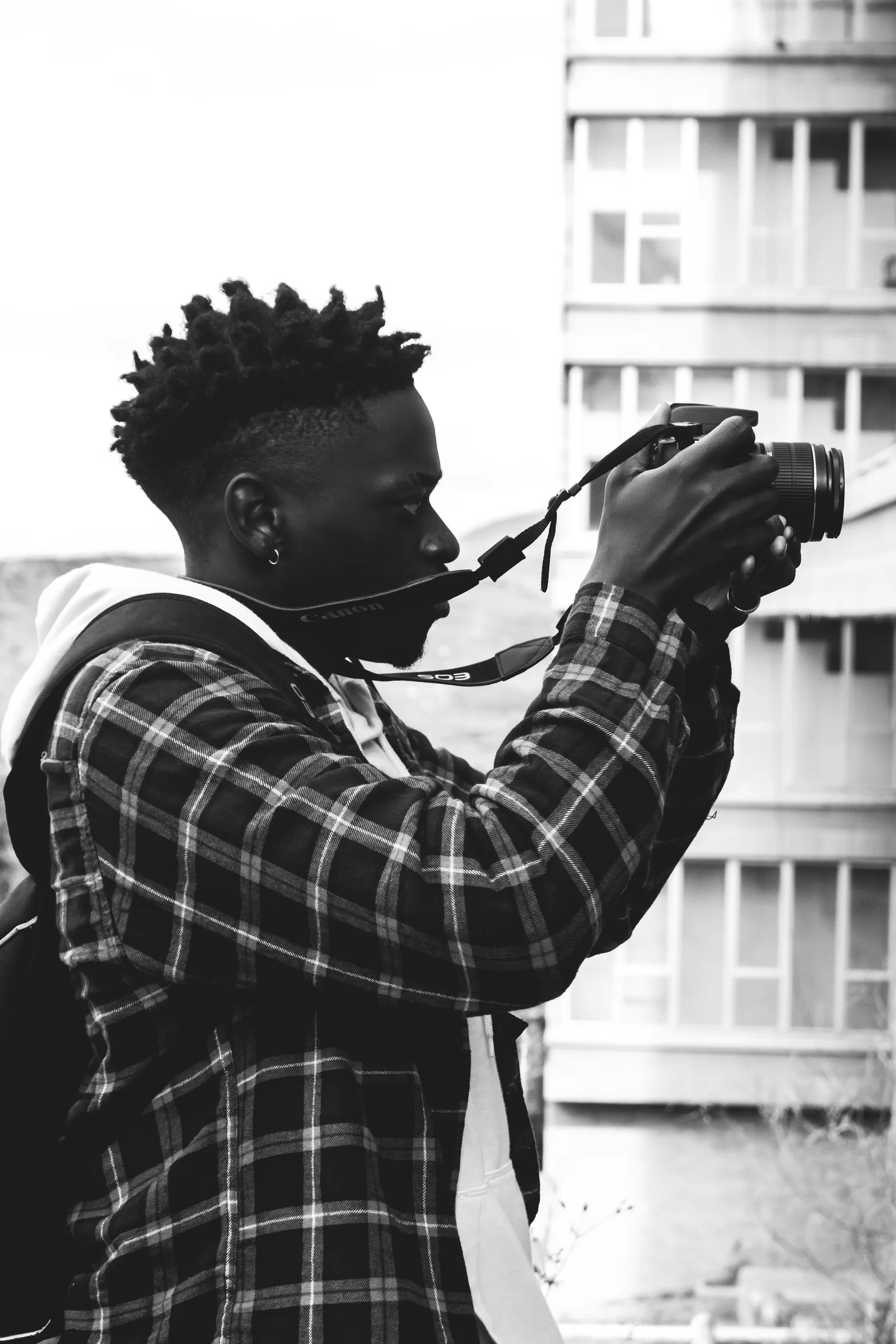 A black and white photo of a man in a plaid shirt taking a picture outdoors
