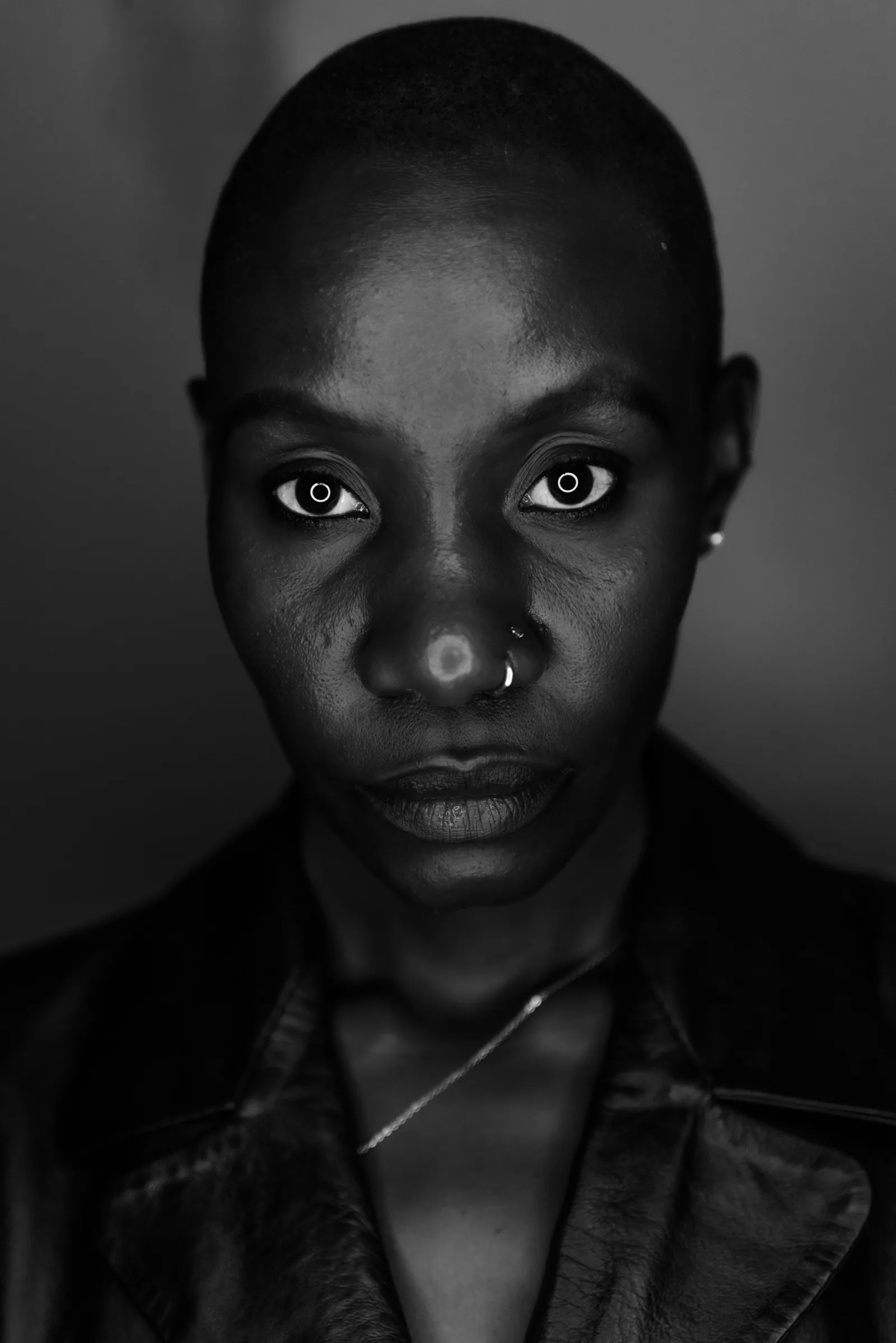 A black and white studio portrait of a woman with a shaved head, lit from one side