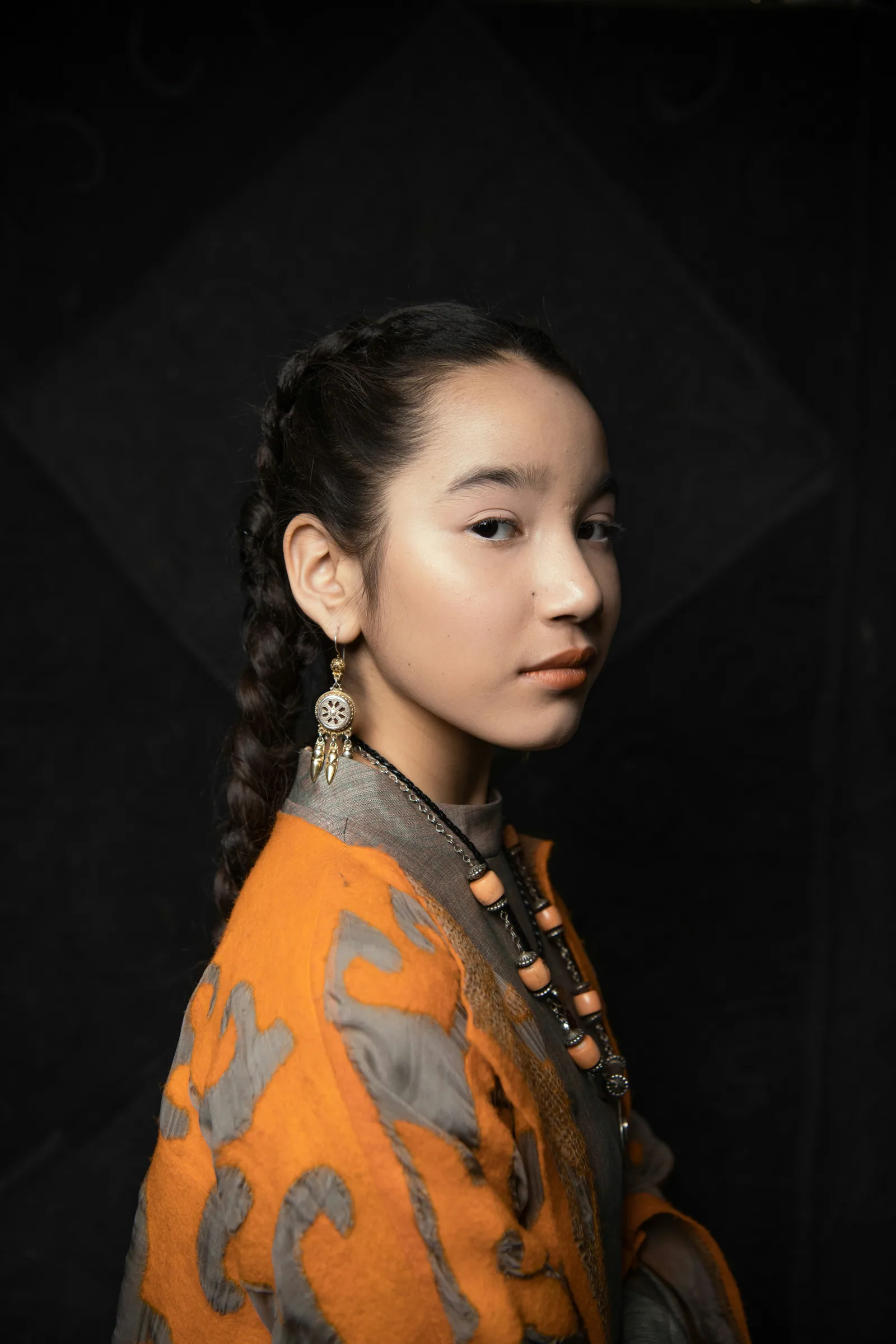 A colour portrait of a young woman in an orange and blue dress against a dark backdrop