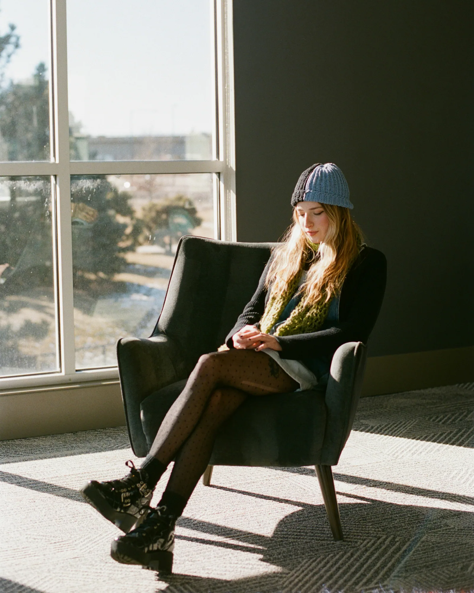 Young woman in hat sits in armchair by window