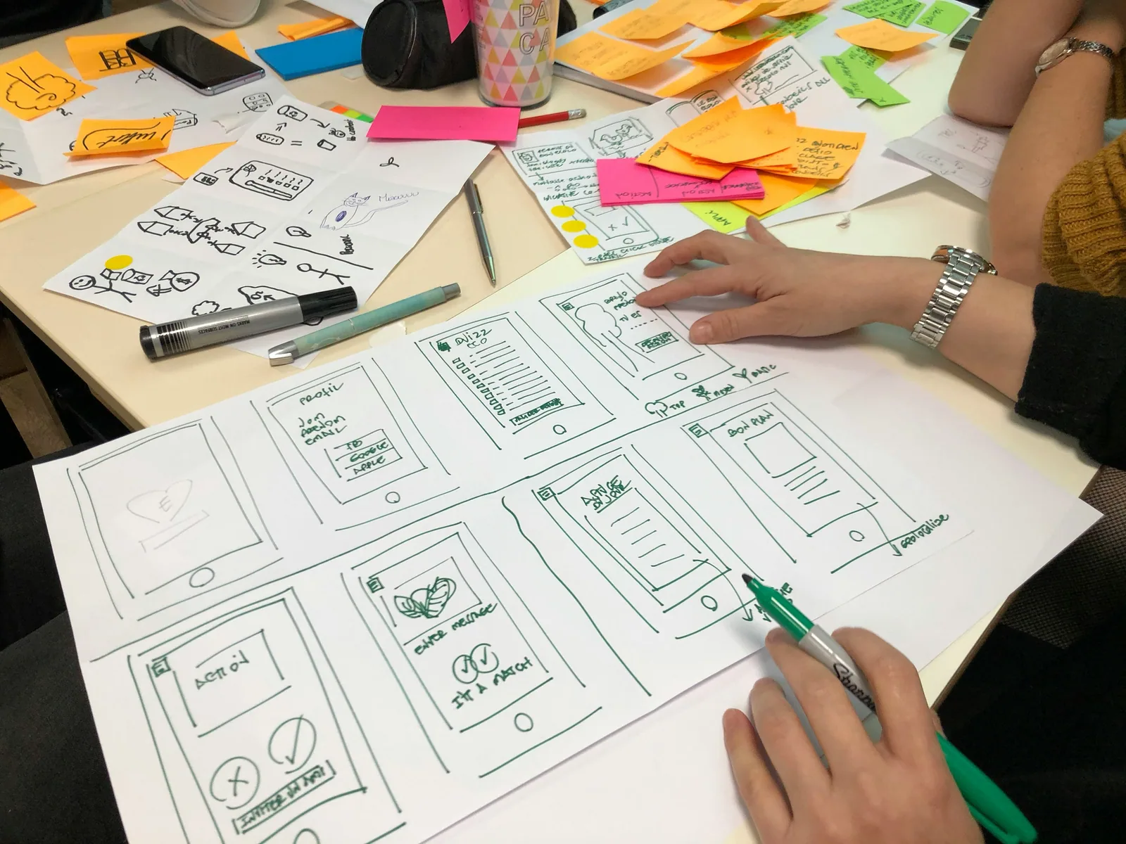 Hands sketching screen layouts on paper among sticky notes