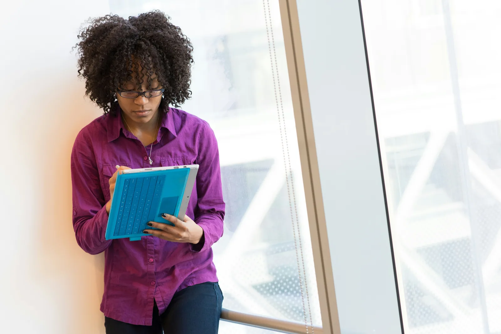 A woman in a purple shirt planning on a tablet by a window