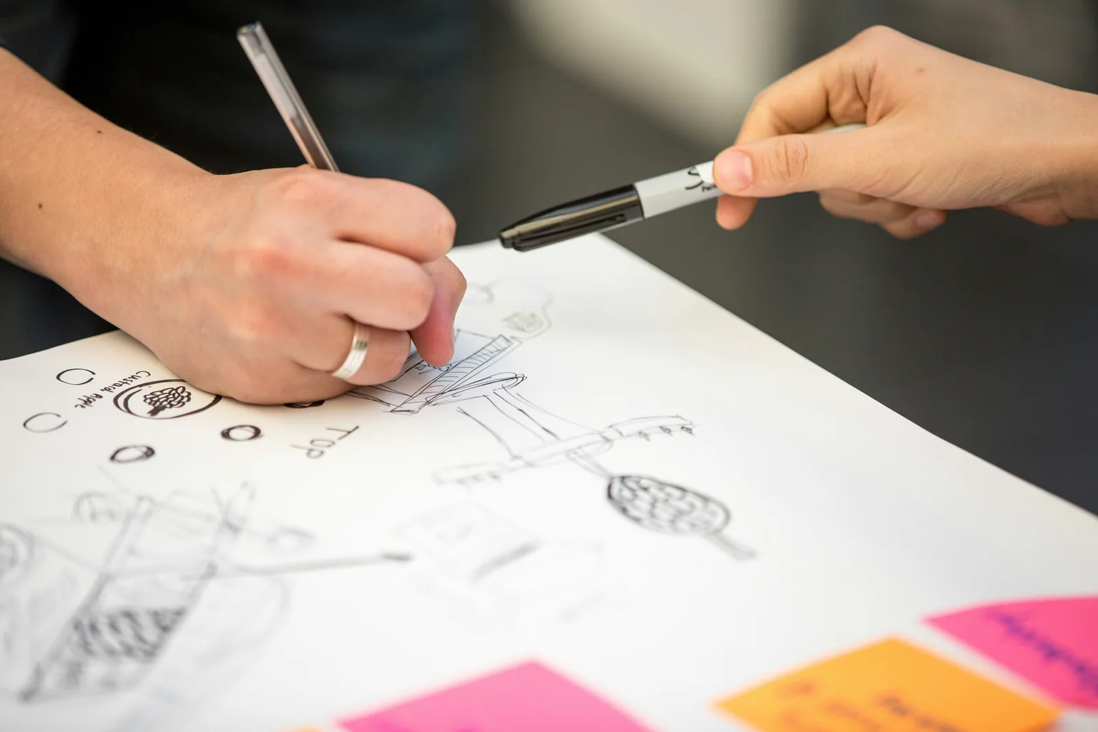 Two hands sketching on paper with sticky notes beside them