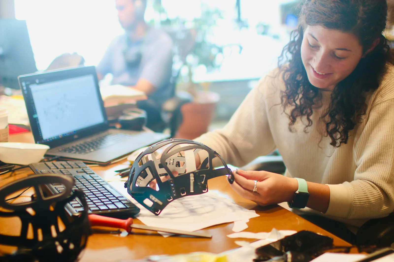 A woman testing a hardware prototype at a busy desk