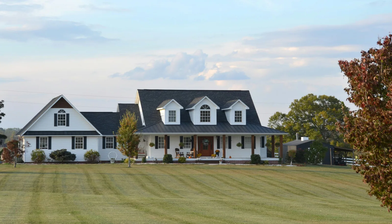 A large white farmhouse with a wrap-around porch and land
