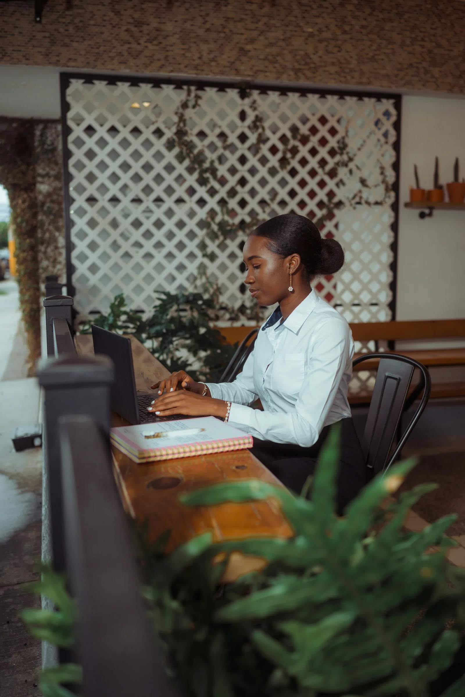 A woman working on a laptop at a desk in a warm, plant-filled room