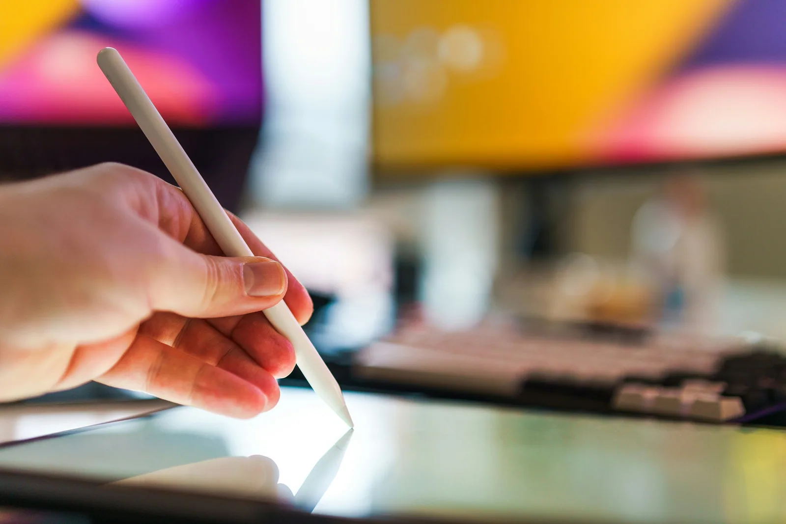 A stylus drawing on a tablet in front of bright colours
