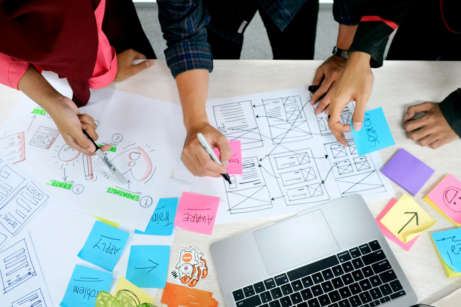 Hands sketching wireframes among sticky notes and a laptop