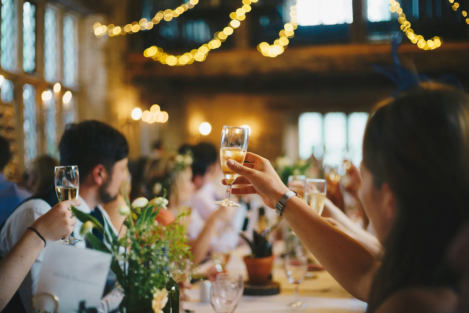 Guests raising glasses in a hall strung with warm lights