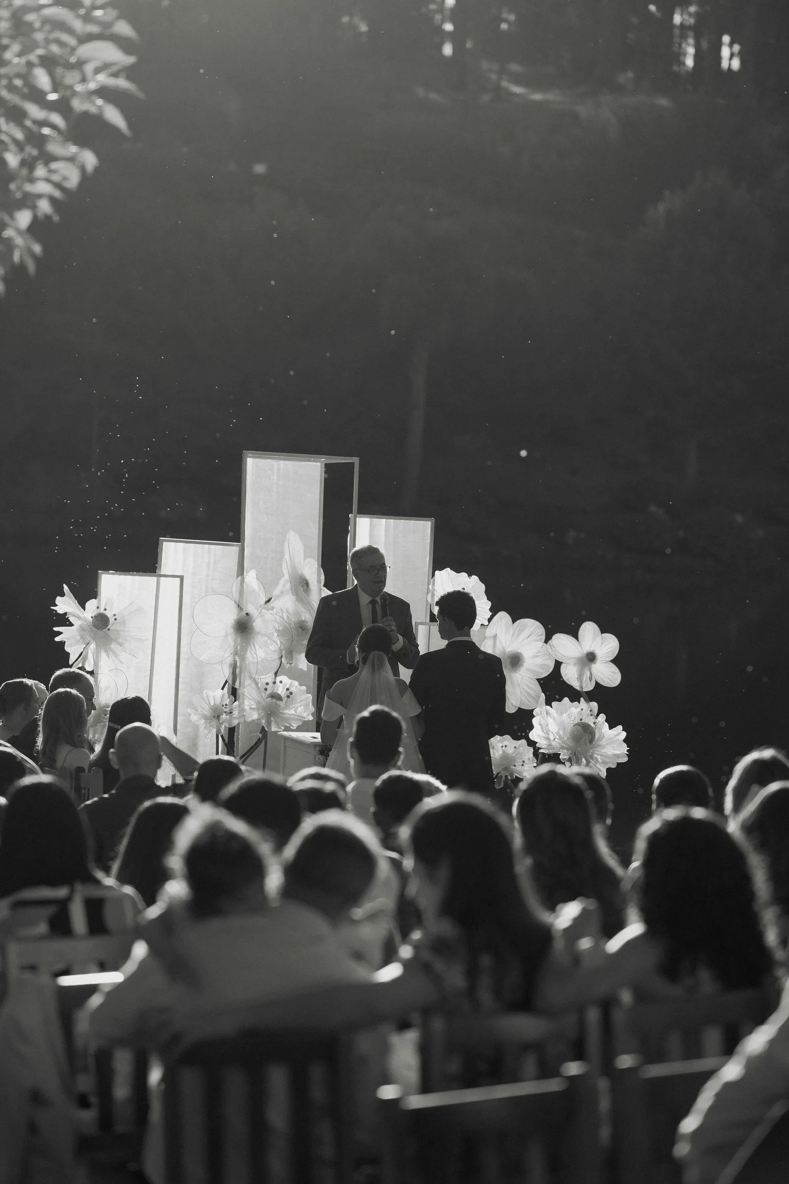 A black and white outdoor ceremony, guests seated under the trees