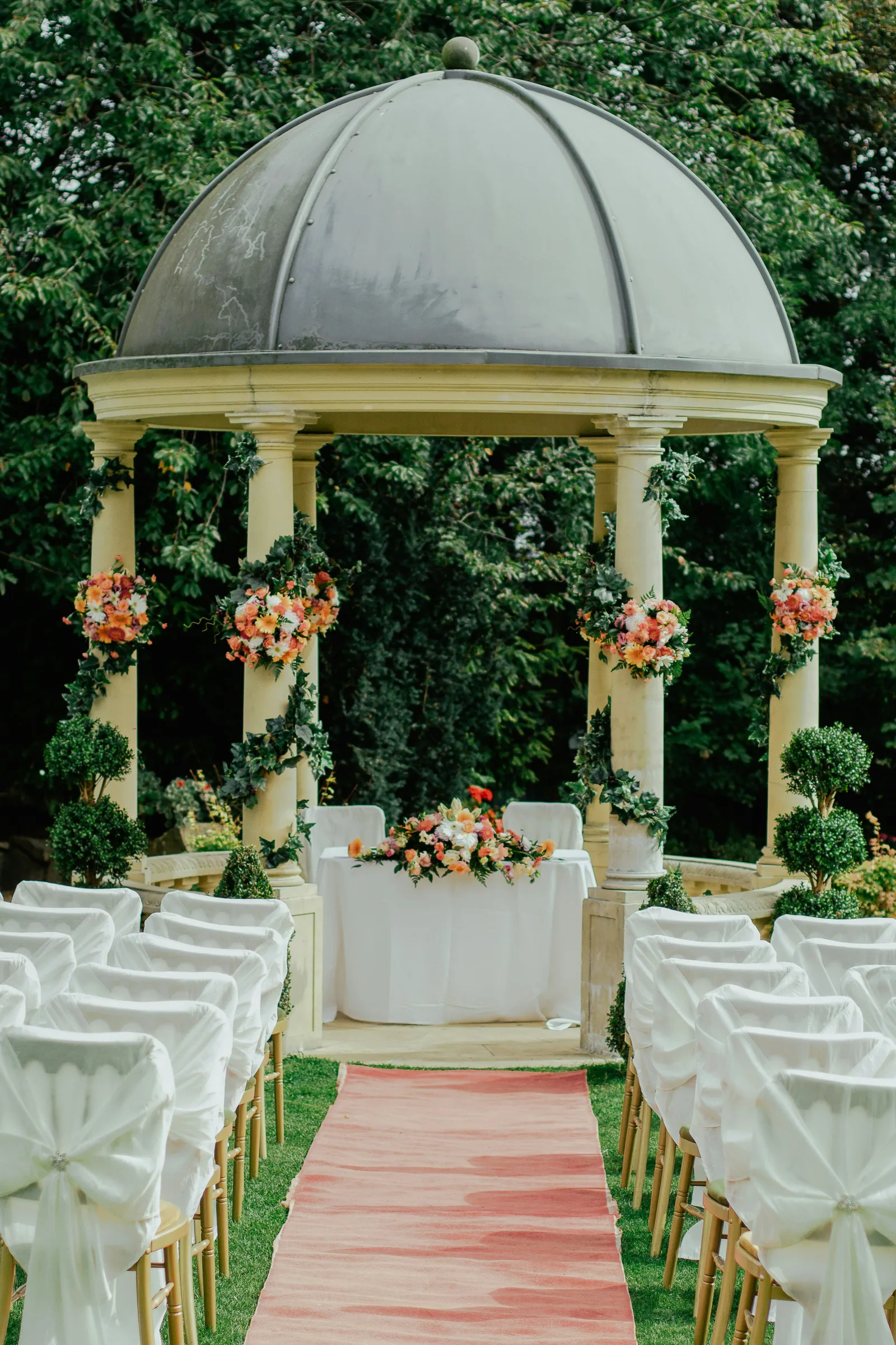 A garden gazebo with rows of covered chairs and a pink aisle