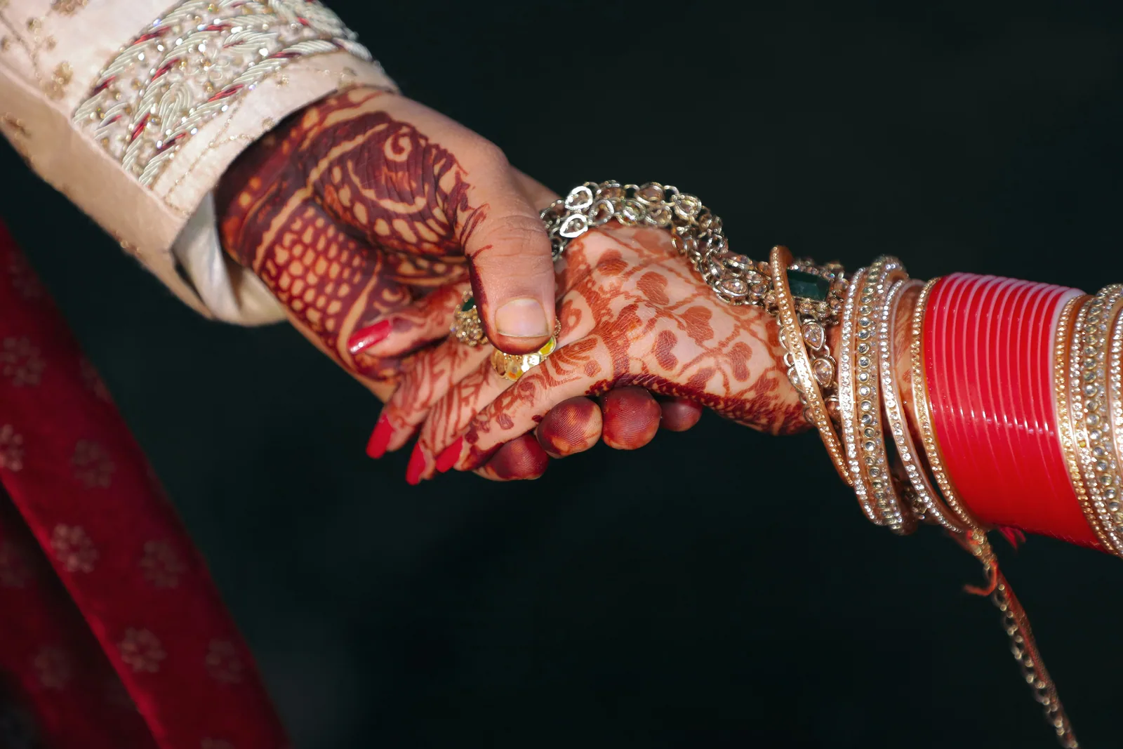 Two hands with henna and red bangles holding each other