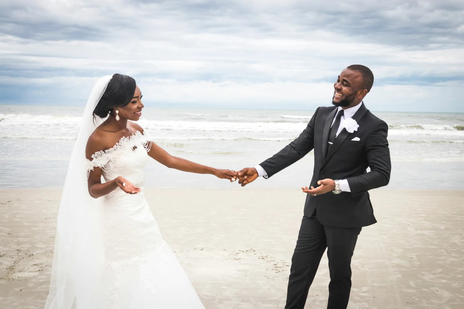 A bride and groom holding hands and laughing on a beach
