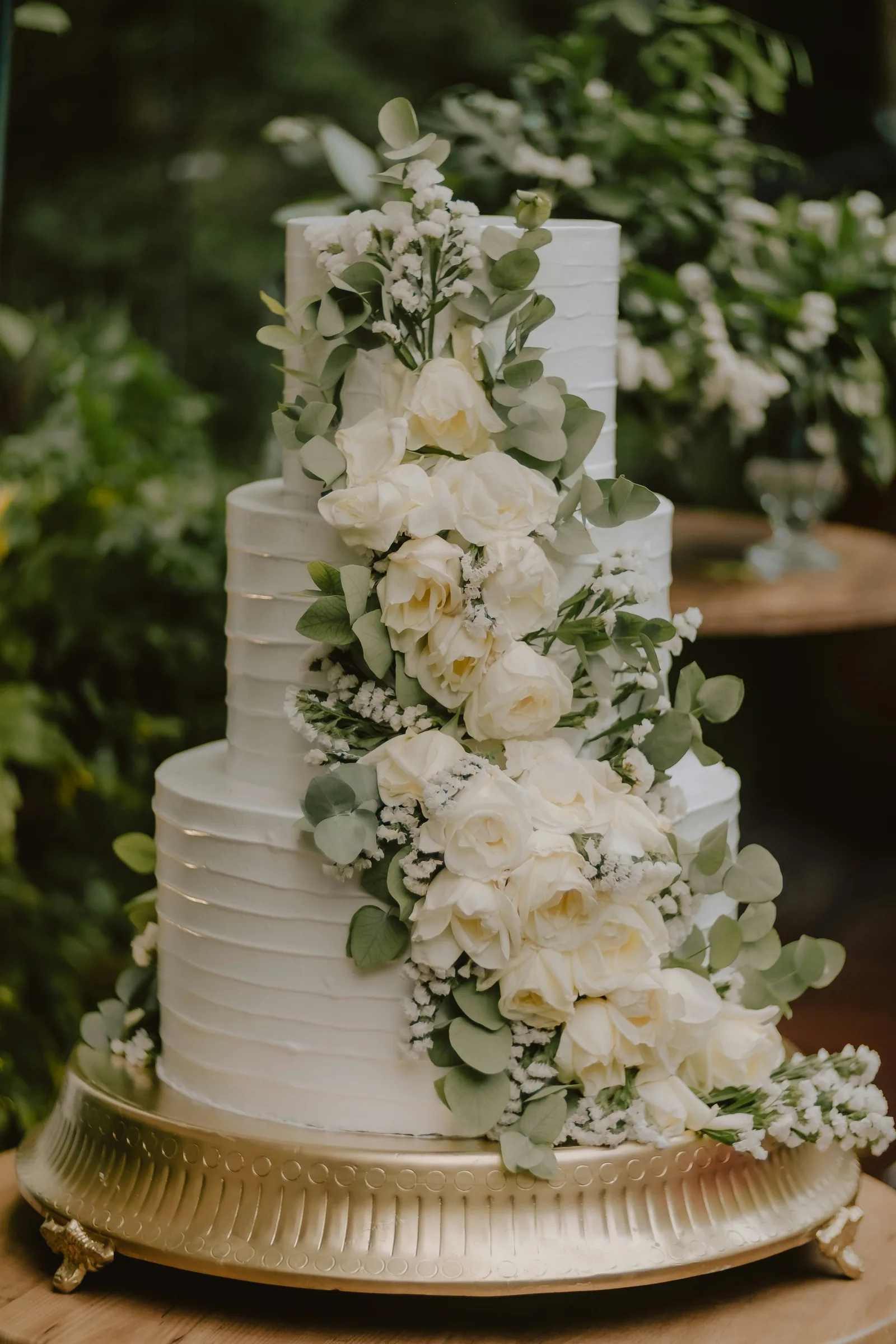 A tall white cake covered in white flowers and greenery