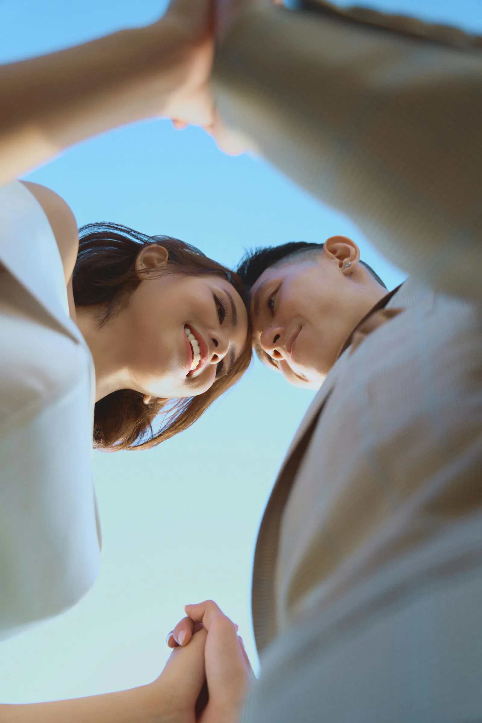 A couple seen from below, leaning in, against a blue sky